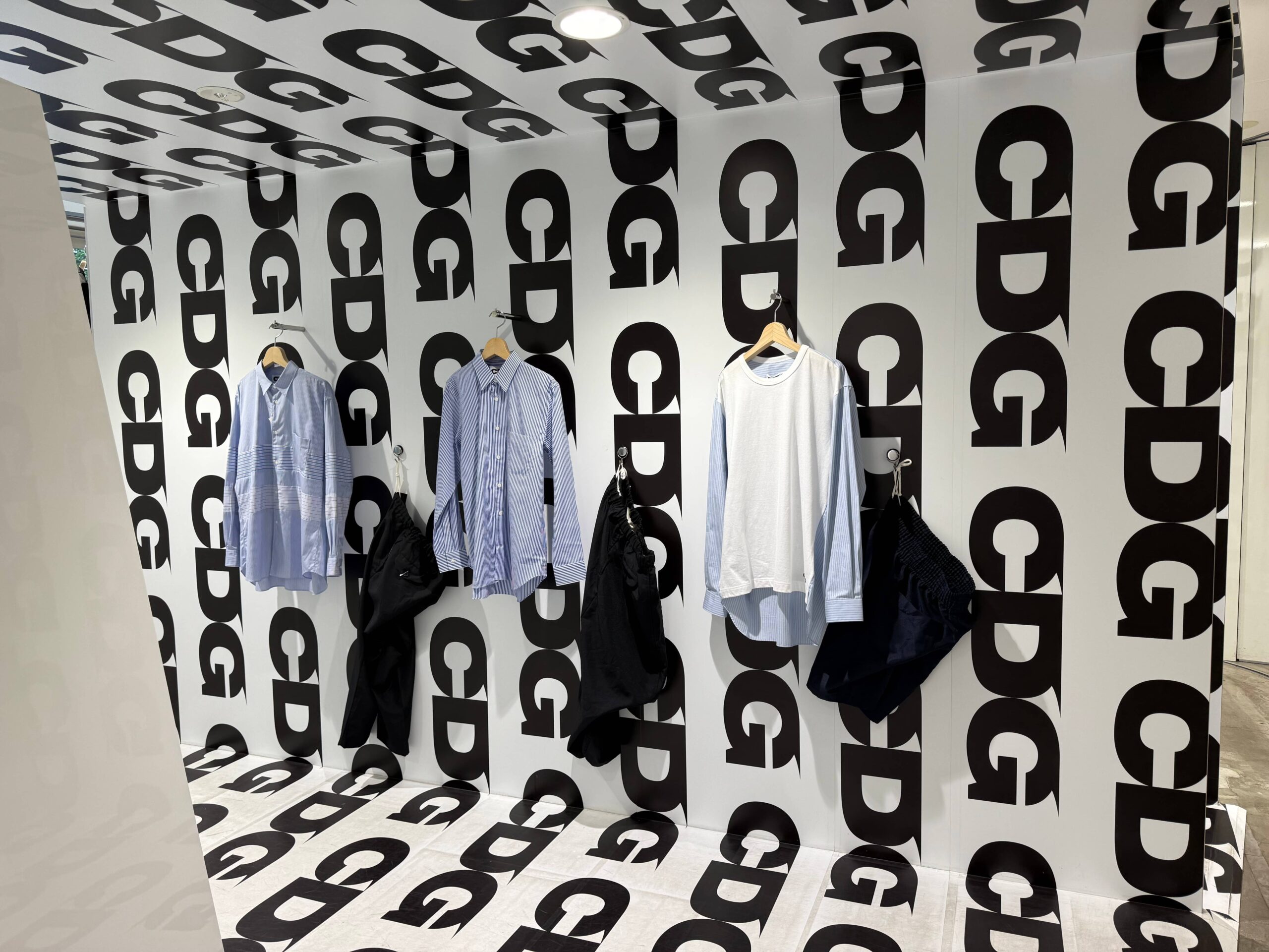 CDG store wall display shirts and pants with CDG logo background