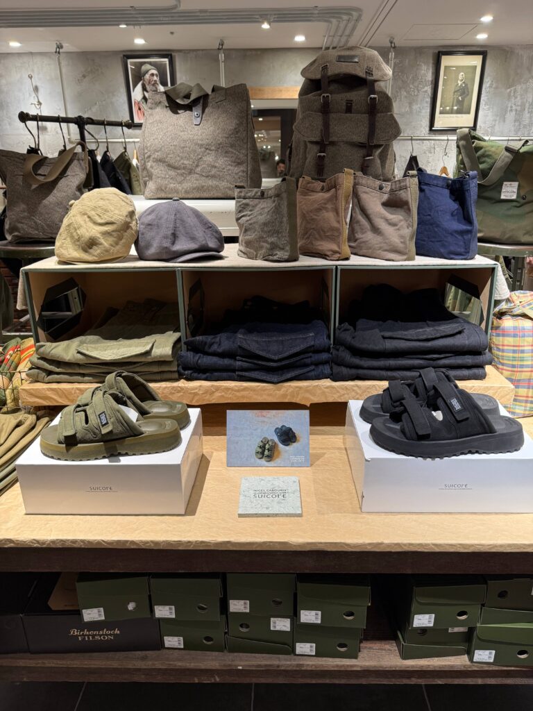 Nigel Cabourn store display shelf with Swiss Army bags, Suicoke collaboration sandals, British Army Pants, and black denim