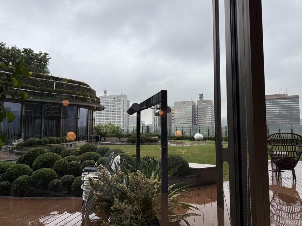 雨の日のカフェの窓から見える、テーブルと椅子が置かれたガーデンテラス。