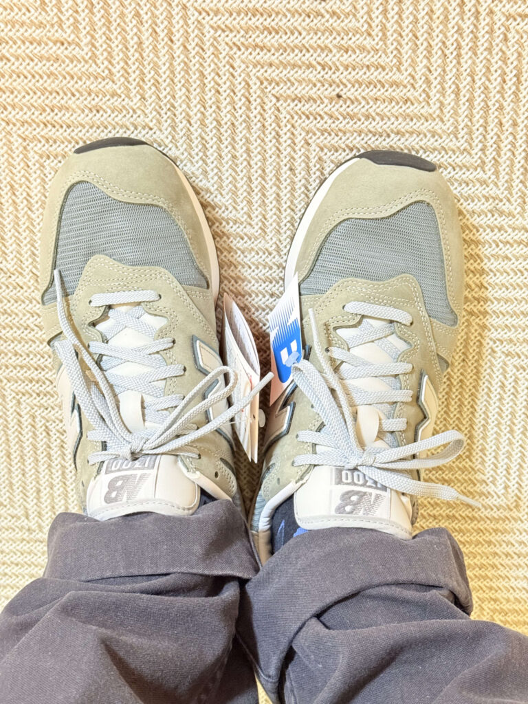 グレーのニューバランスU1300Jスニーカーとブルージーンズを着用した足元の俯瞰ショット。背景はコンクリート。