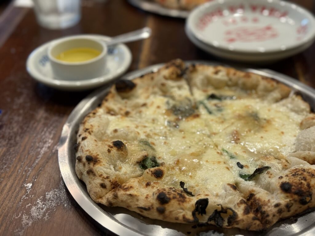 PIZZA DA BABBOのクワトロフォルマッジ。手前にピザ全体が写っており、奥には蜂蜜の入った小瓶が見える。