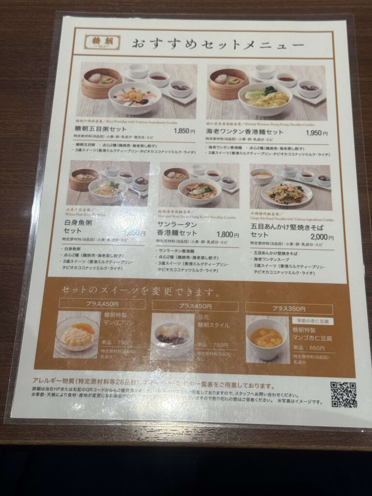 黒いお盆に乗せられた糖朝のサンラータン香港麺セット。赤いスープの麺、セイロに入った点心2種、白いデザート、急須のお茶が並んでいる。
