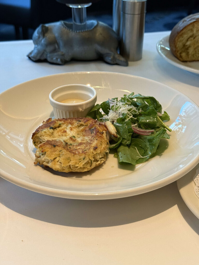 A half-sized crab cake served on a white plate, garnished with a lemon wedge and sauce.
