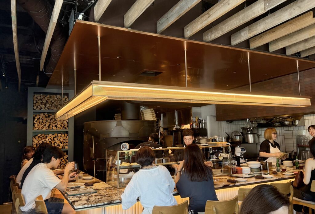 Counter seats arranged around a restaurant's kitchen, with a view of the open kitchen and cooking in progress.