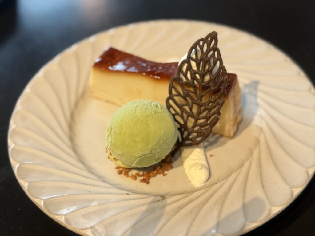 Hojicha (roasted green tea) pudding on a white plate, topped with cream and a mint leaf.