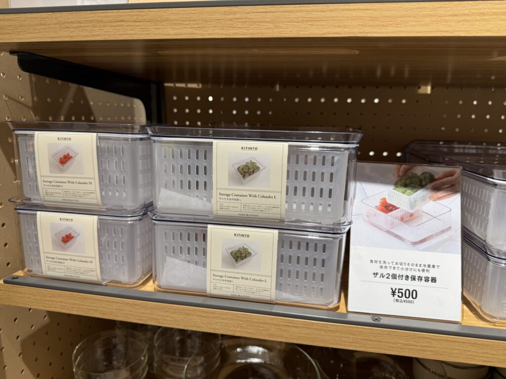 木製ハンドル付きの金属製ザル。中には少量の緑色の野菜が入っている。