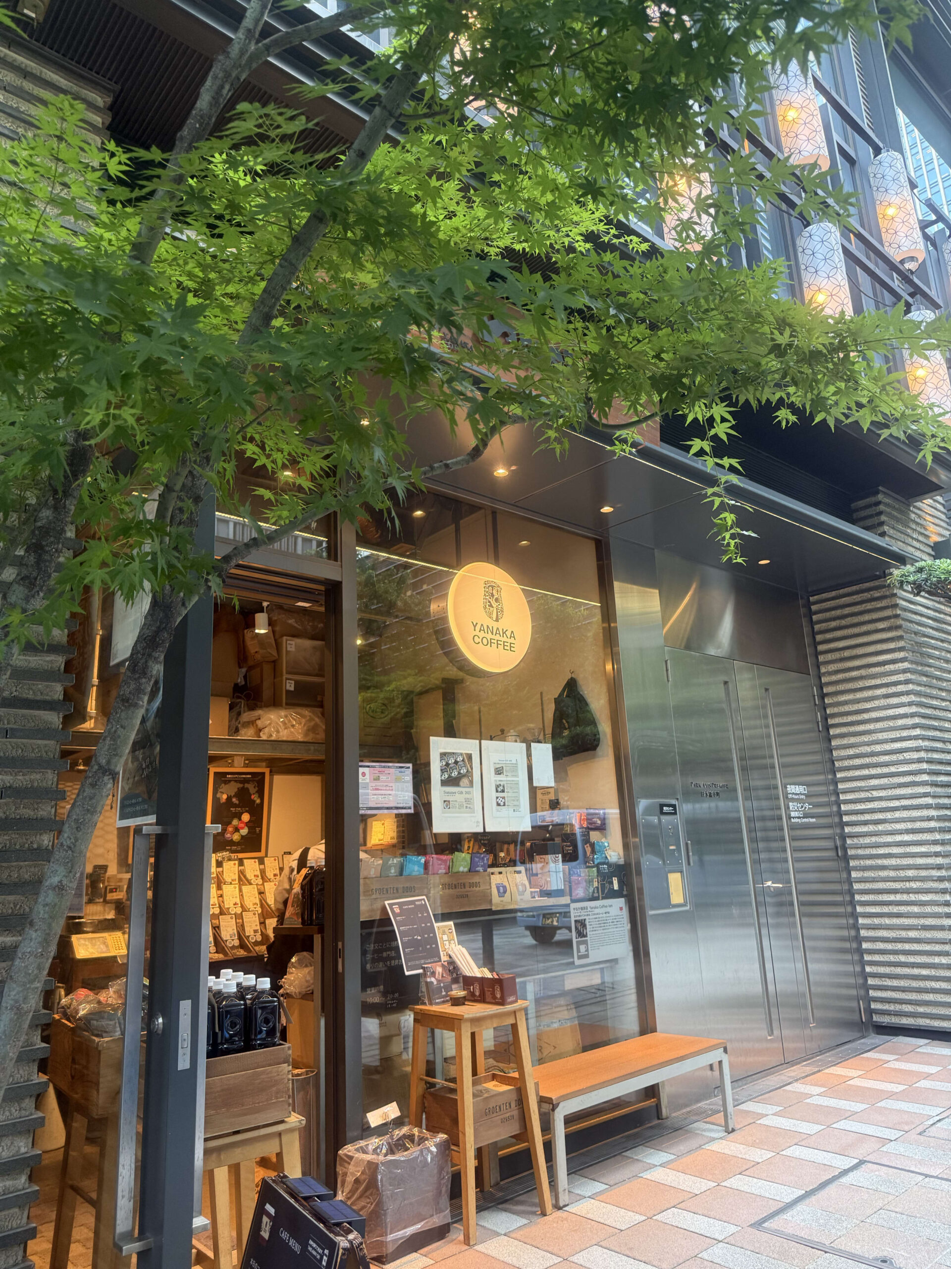 Ynaka Coffeeの緑豊かなエントランス、植物が飾られた都会のカフェの入り口