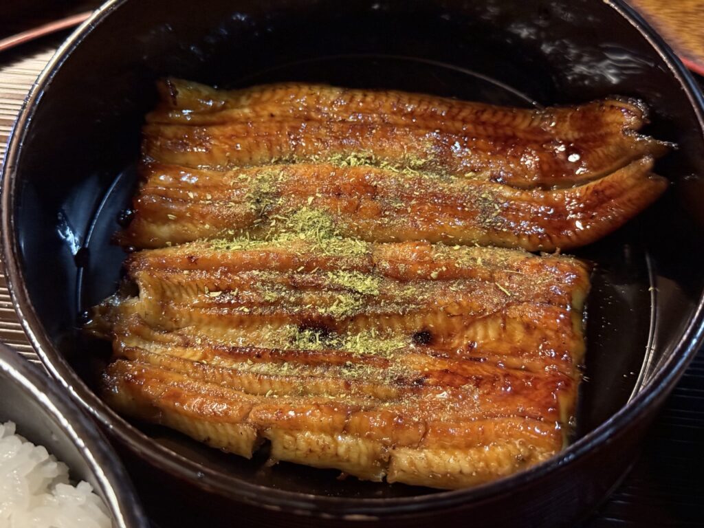 黒い器に盛られた鰻料理に、自家製の山椒が鮮やかに振りかけられているクローズアップ写真。