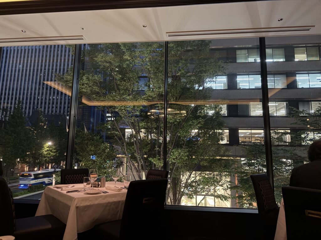 ライトアップされた東京駅丸の内駅舎と、車の光跡が流れる周辺の高層ビル群の夜景。