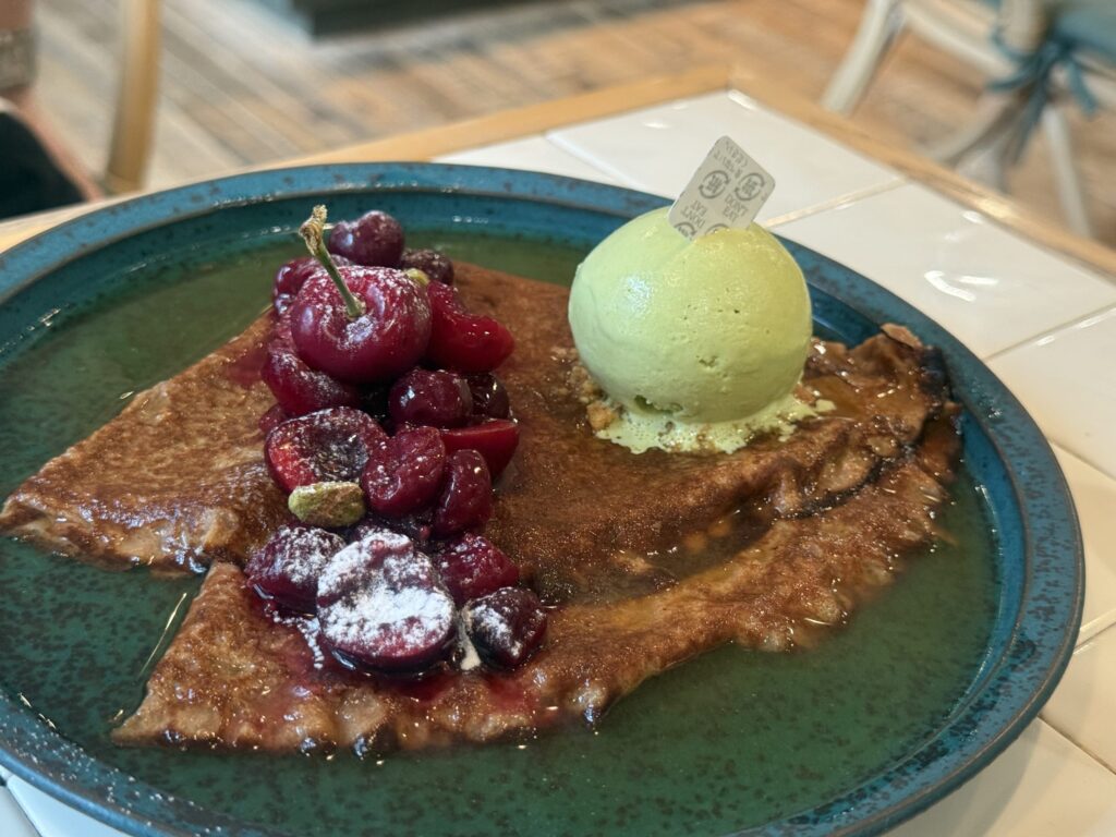 Crêpes Suzette with pistachio gelato and cherries on a white plate.