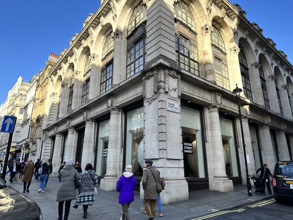 Exterior view of the white, historic building housing Dover Street Market London, showing large windows and an arched entrance.