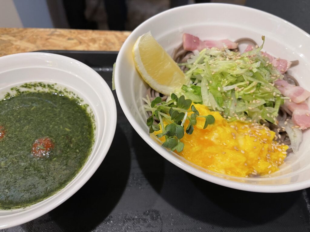 鮮やかな緑色のバジルペーストがたっぷりかかった、珍しいバジル蕎麦のクローズアップ