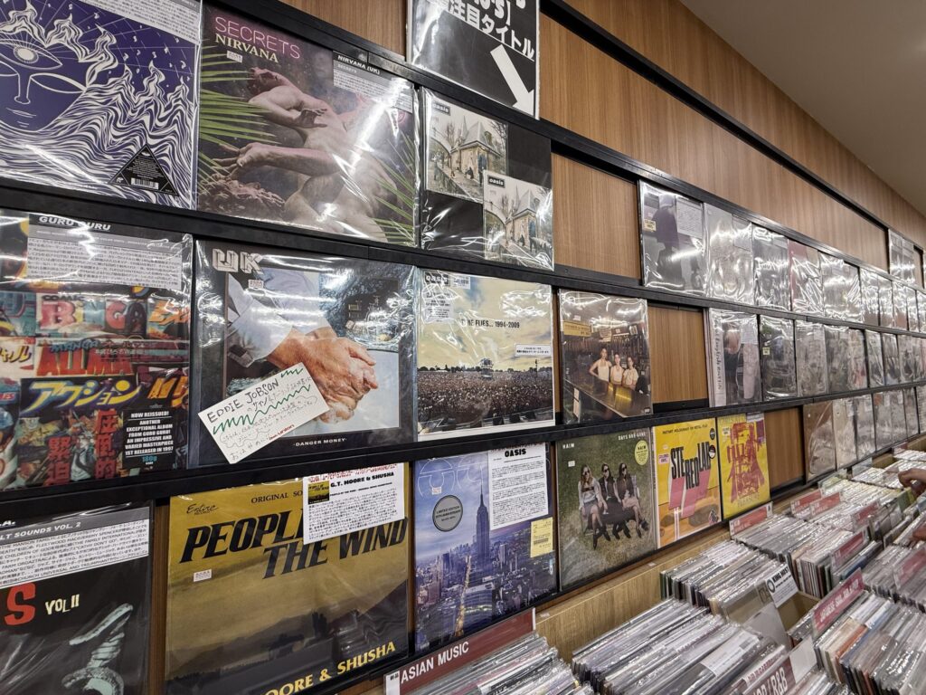 レコード店の新品レコードコーナーの棚に、色とりどりのジャケットのレコードが多数陳列されている様子。