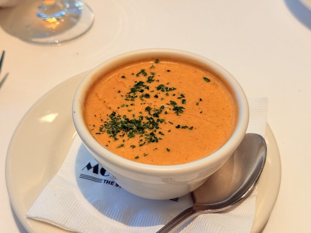 Rich lobster bisque soup in a white bowl, garnished with parsley.