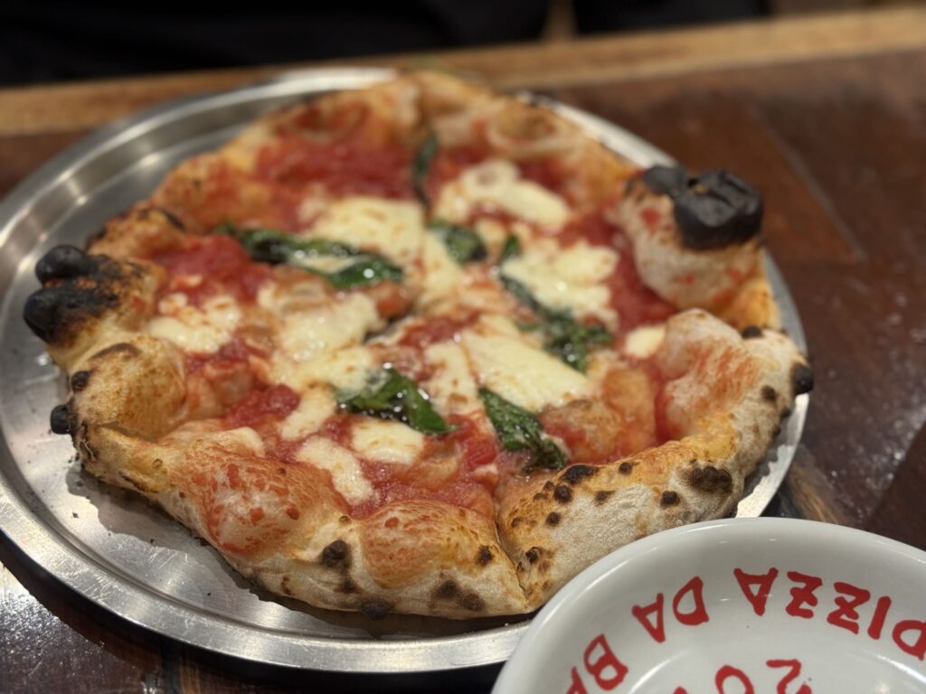 PIZZA DA BABBOのマルゲリータピザ。木製のピールに乗っており、トマトソース、モッツァレラチーズ、バジルの葉が特徴的。
