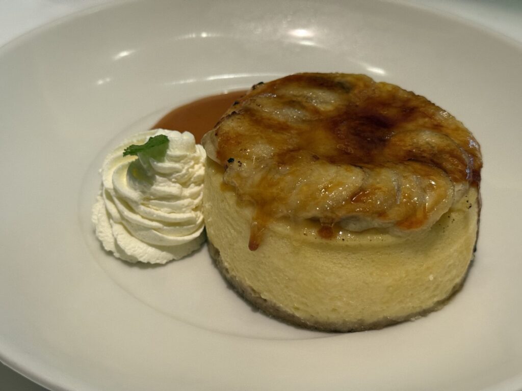 A slice of New York cheesecake on a white plate on a wooden table, with a fork resting beside it.