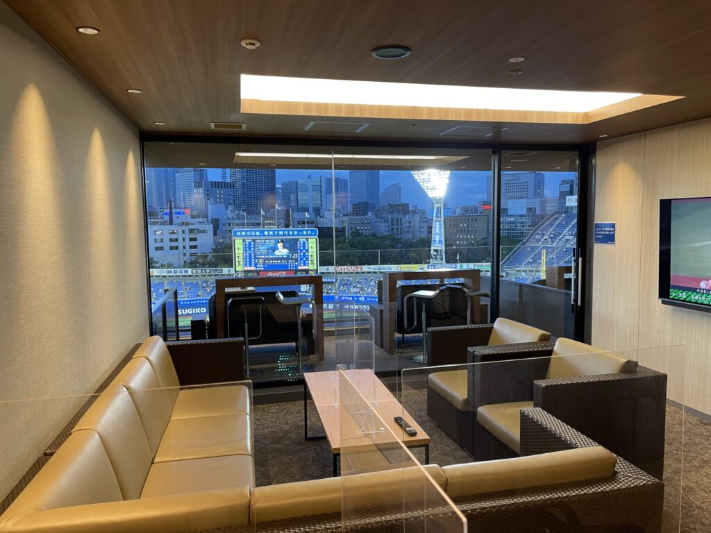 A view of a room where people are gathered around a table, eating and drinking while watching sports on a large monitor.