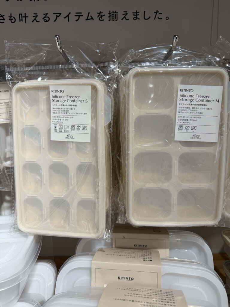 A green silicone freezer storage container with a blue lid, featuring six compartments, some of which contain frozen food, placed on a white background.