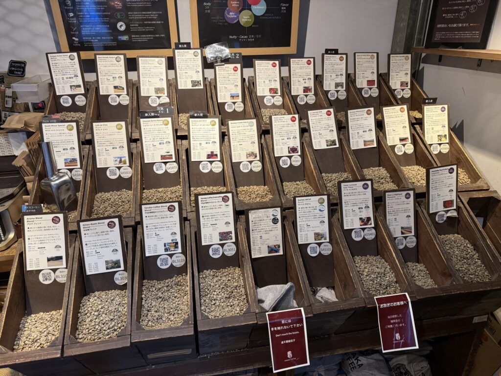 Hessian sacks filled with various types of green coffee beans, densely arranged on wooden shelves.
