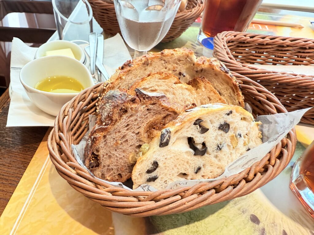 A basket filled with several types of bread placed on a wooden table.
