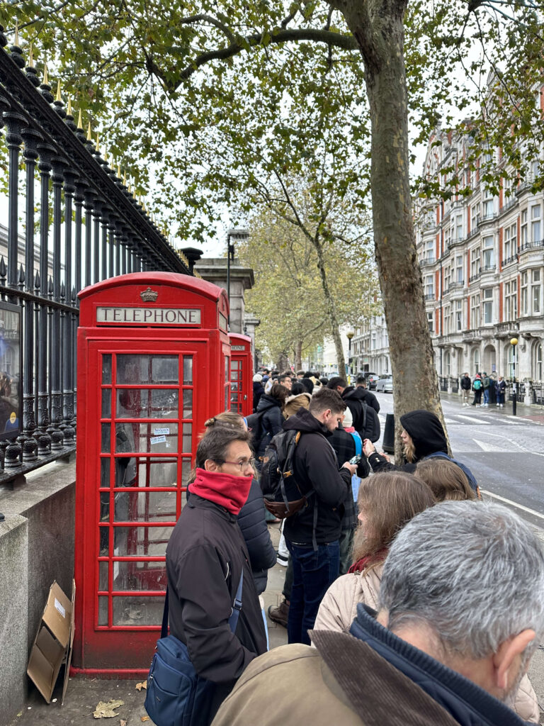 ロンドンの大英博物館の壮大な正面玄関の前で、開館を待つ観光客が長い列をなしている朝の風景。