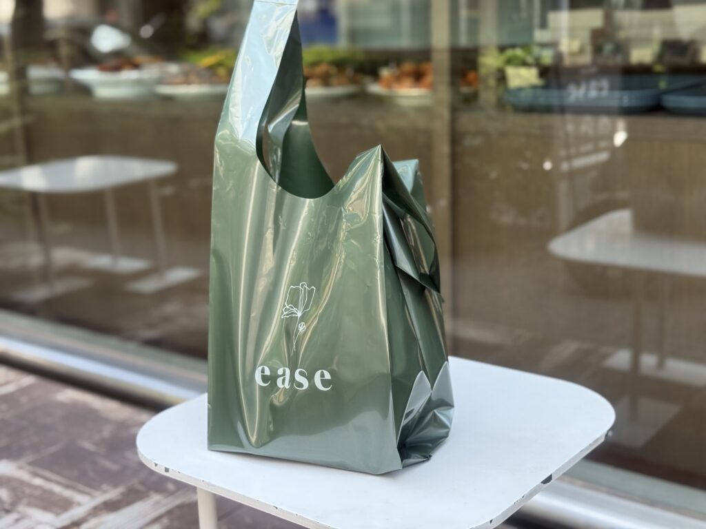 A person's hand holding a white paper bag filled with baked goods, with a scone-like pastry visible inside.