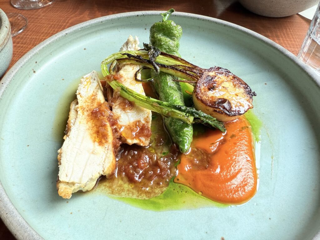 Raw Tamba black chicken, green Manganji peppers, and red and yellow bell peppers placed on a white plate.