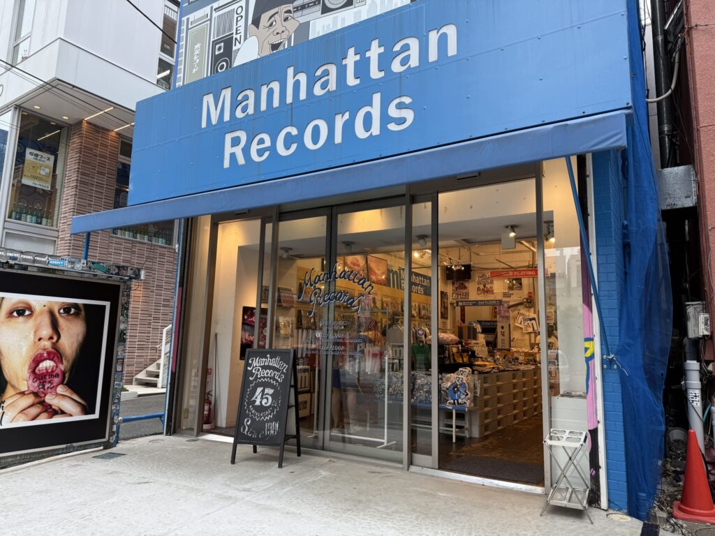 The exterior of the long-established record store 'Manhattan Records' in Shibuya, featuring its distinctive red sign.