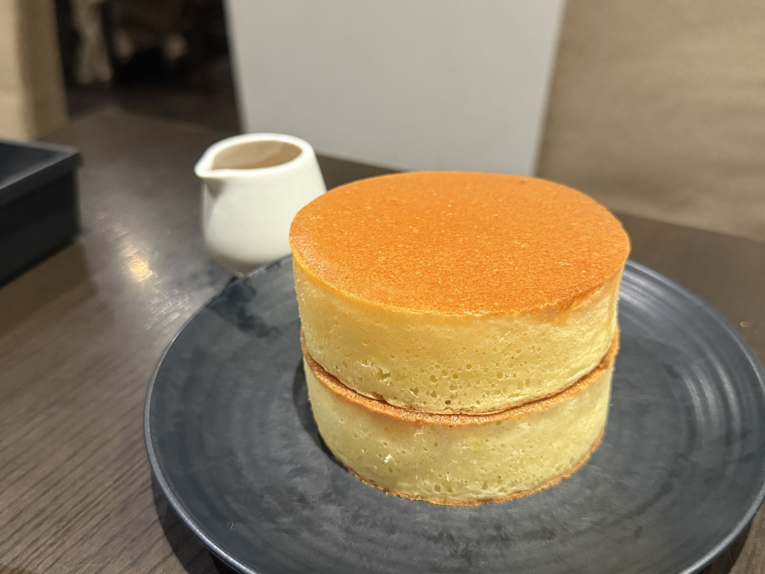 白いお皿の上に乗った、バターとシロップがかかっている分厚い3段重ねのホットケーキ。