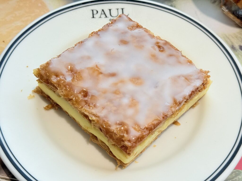 A mille-feuille pastry dusted with powdered sugar on a white plate, with a fork placed beside it.