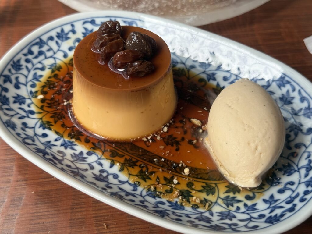 A custard pudding with whipped cream and a mint leaf on a white plate, surrounded by caramel sauce.