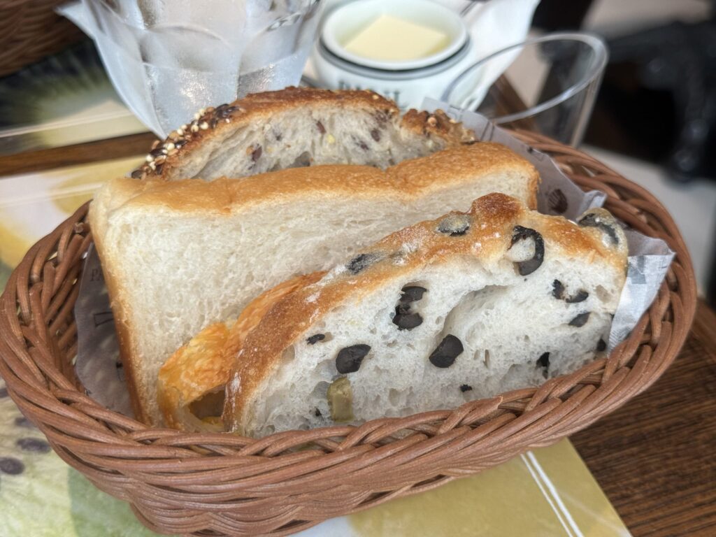 A white plate on a wooden table, holding a second helping of various types of bread.