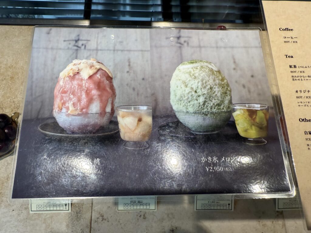 暗いテーブルの上に置かれた白い器に盛られた、Patisserie easeのかき氷。上には濃厚なソースとナッツのようなトッピングが乗っている。