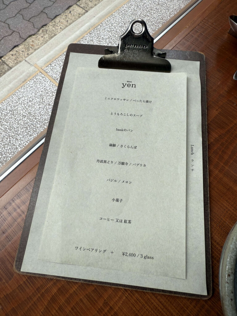 A Japanese 'oshinagaki' (course menu) written in brush script, placed on a wooden table, listing the dishes for a traditional meal.