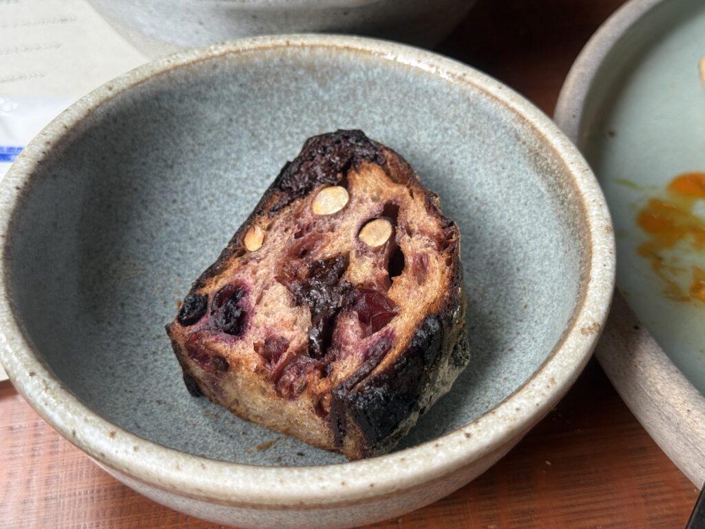 A slice of rustic bread with figs and chocolate on a white plate, placed on a wooden table.