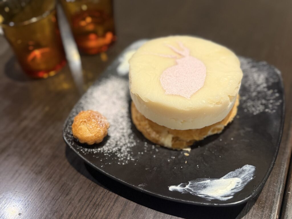A square piece of 'Miji Pie', a seasonal dessert, on a white plate, topped with powdered sugar and a sprig of mint.