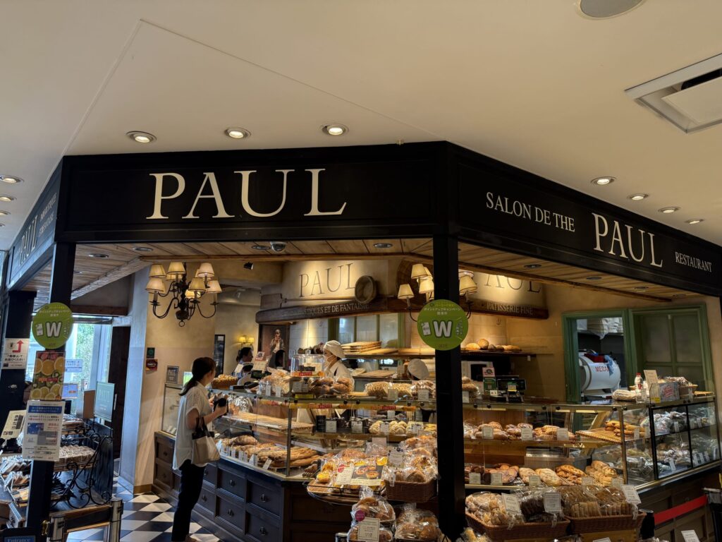 The exterior of the PAUL bakery inside Atré Yotsuya, featuring black awnings and large display windows filled with bread.