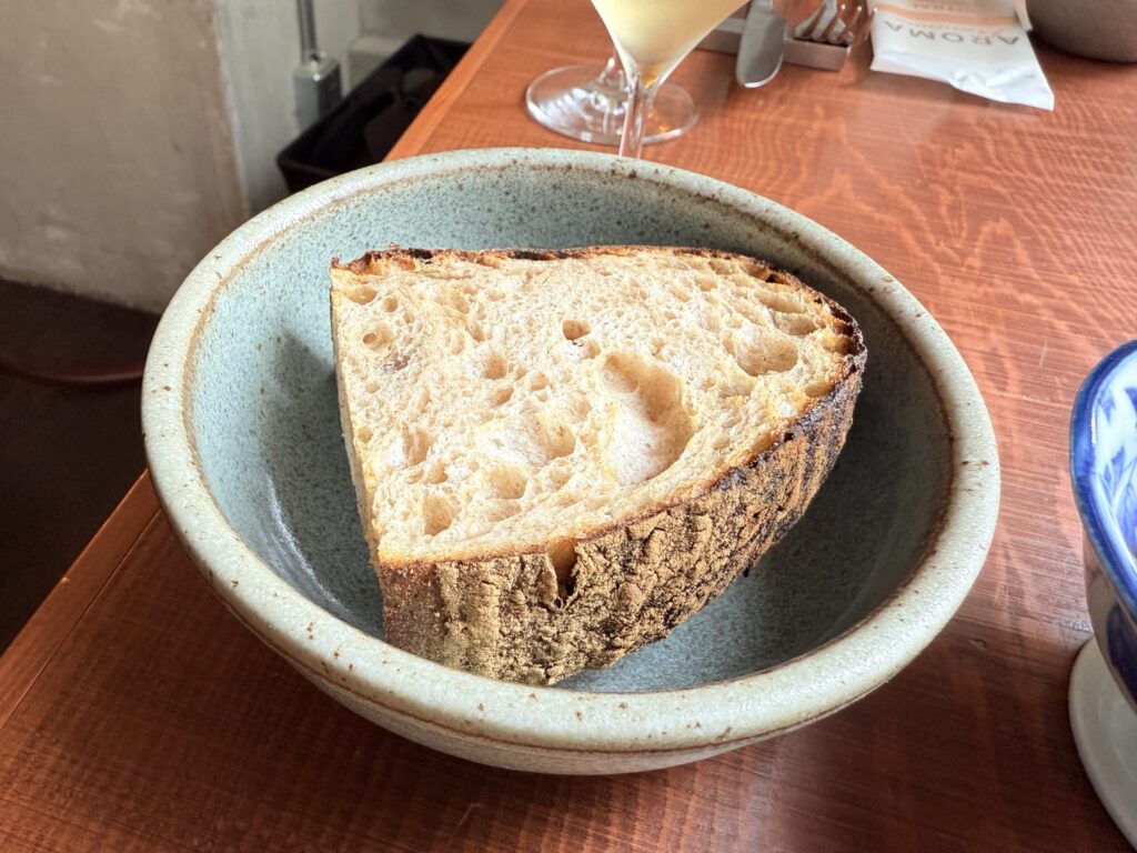 Warm bread, including a round roll and a longer piece, served on a white plate on a wooden table.