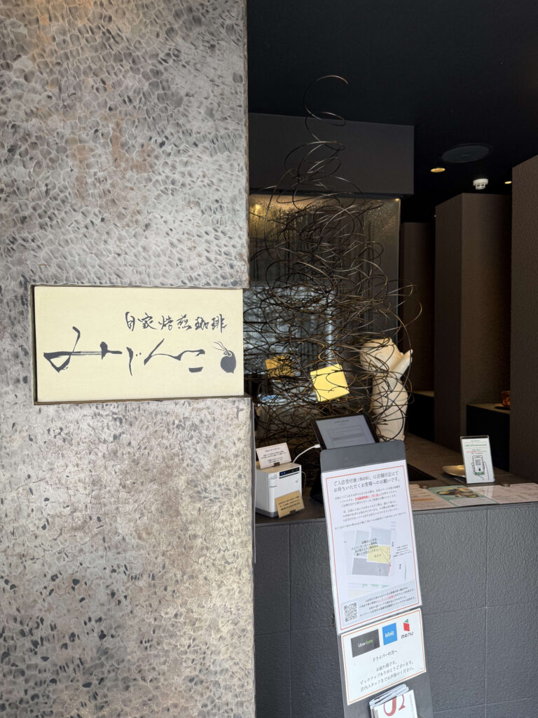 自家焙煎珈琲みじんこのエントランスに置かれた、手書きのイラストとメニューが描かれた黒板の看板と、その隣にあるウェイティング用の発券機。