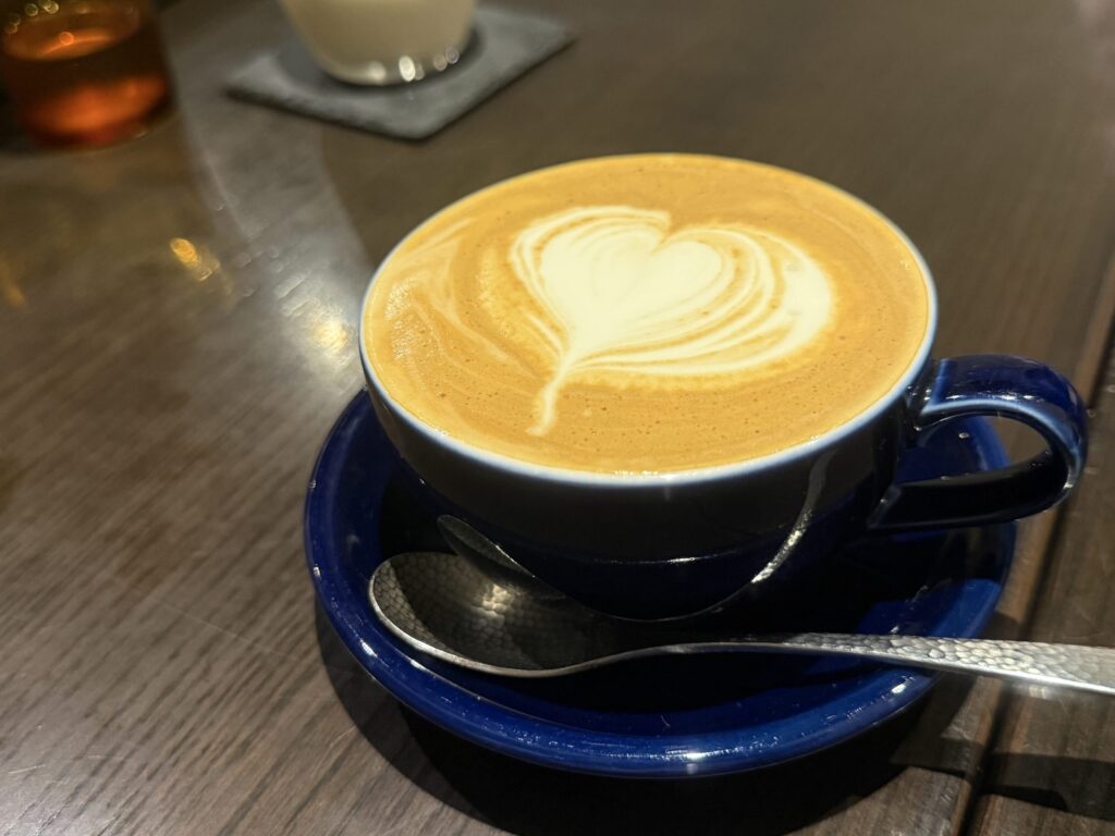 木目のテーブルの上に置かれた、ハートのラテアートが施された白いカップ入りの温かいデカフェ豆乳ラテ。