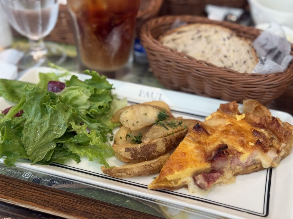 A slice of golden-brown quiche and a side salad with cherry tomatoes and leafy greens are arranged on a white plate, which sits on a wooden table.