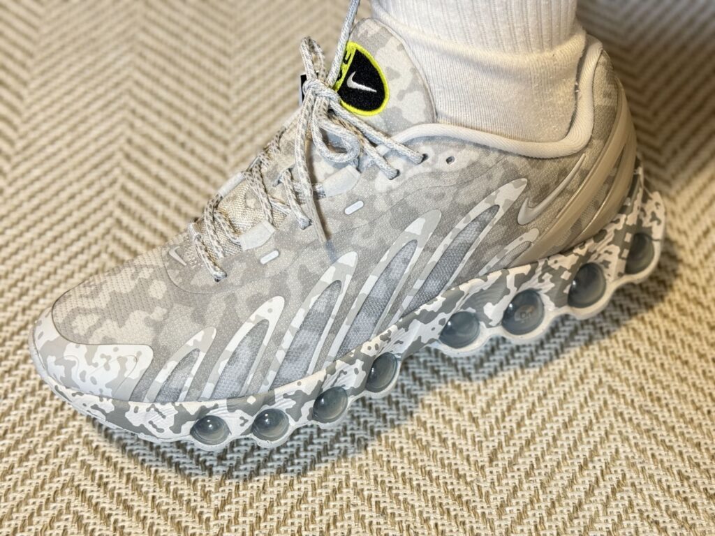 グレーと白の迷彩柄が特徴的なナイキのスニーカーを履いた足元のクローズアップ。背景はヘリンボーン柄のラグ。