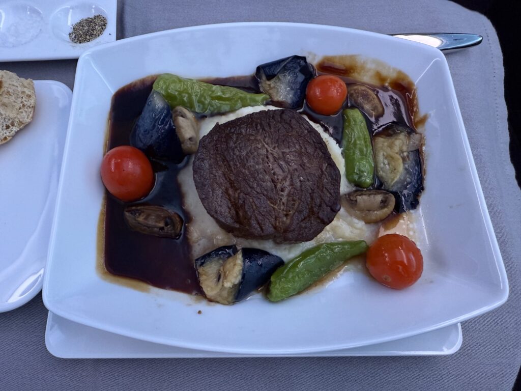 黒い皿に盛り付けられた、ミディアムレアにスライスされた牛フィレステーキ。ソースと焼き野菜が添えられている。