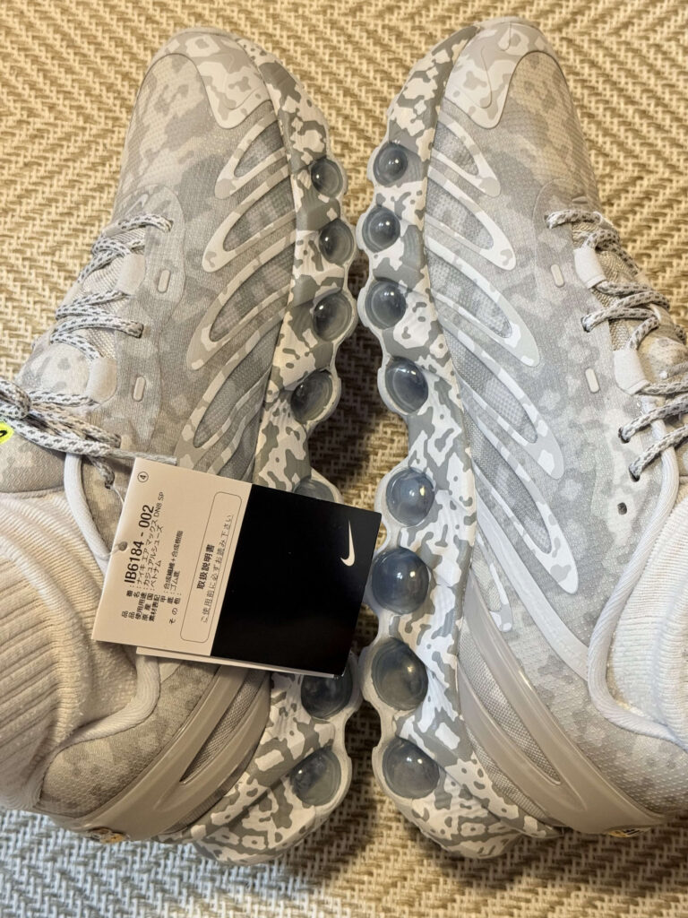 A photo of the Nike Air Max DN8 SP sneakers, featuring a light gray camouflage pattern. The shot focuses on the inner side, showcasing the distinctive Air units.