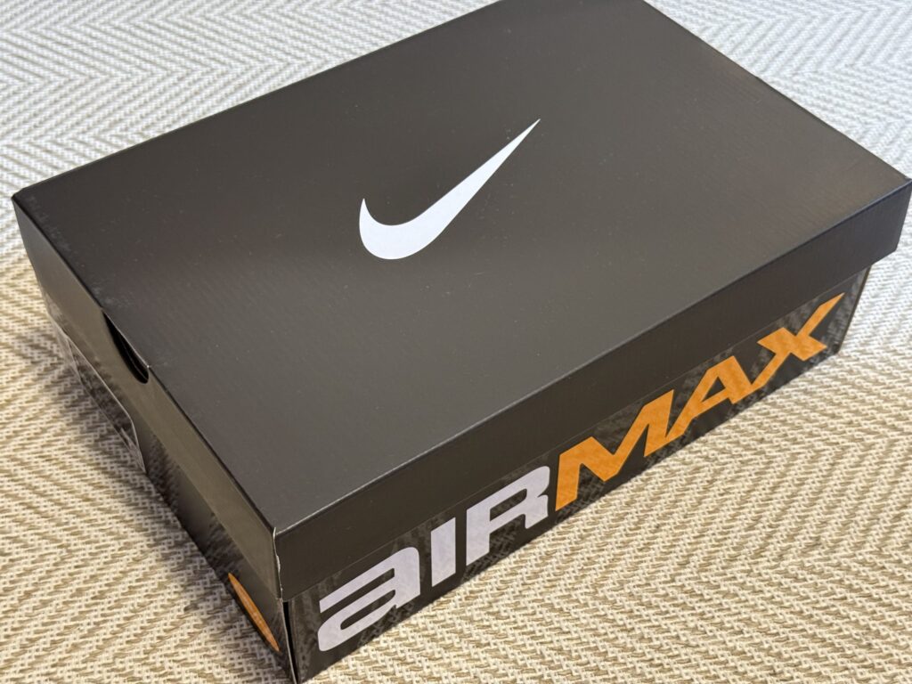 C.EとNikeのコラボスニーカー、Air Max DN8 SPの黒い外箱。蓋には白いスウッシュ、側面にはオレンジと白のAIRMAXロゴがデザインされている。