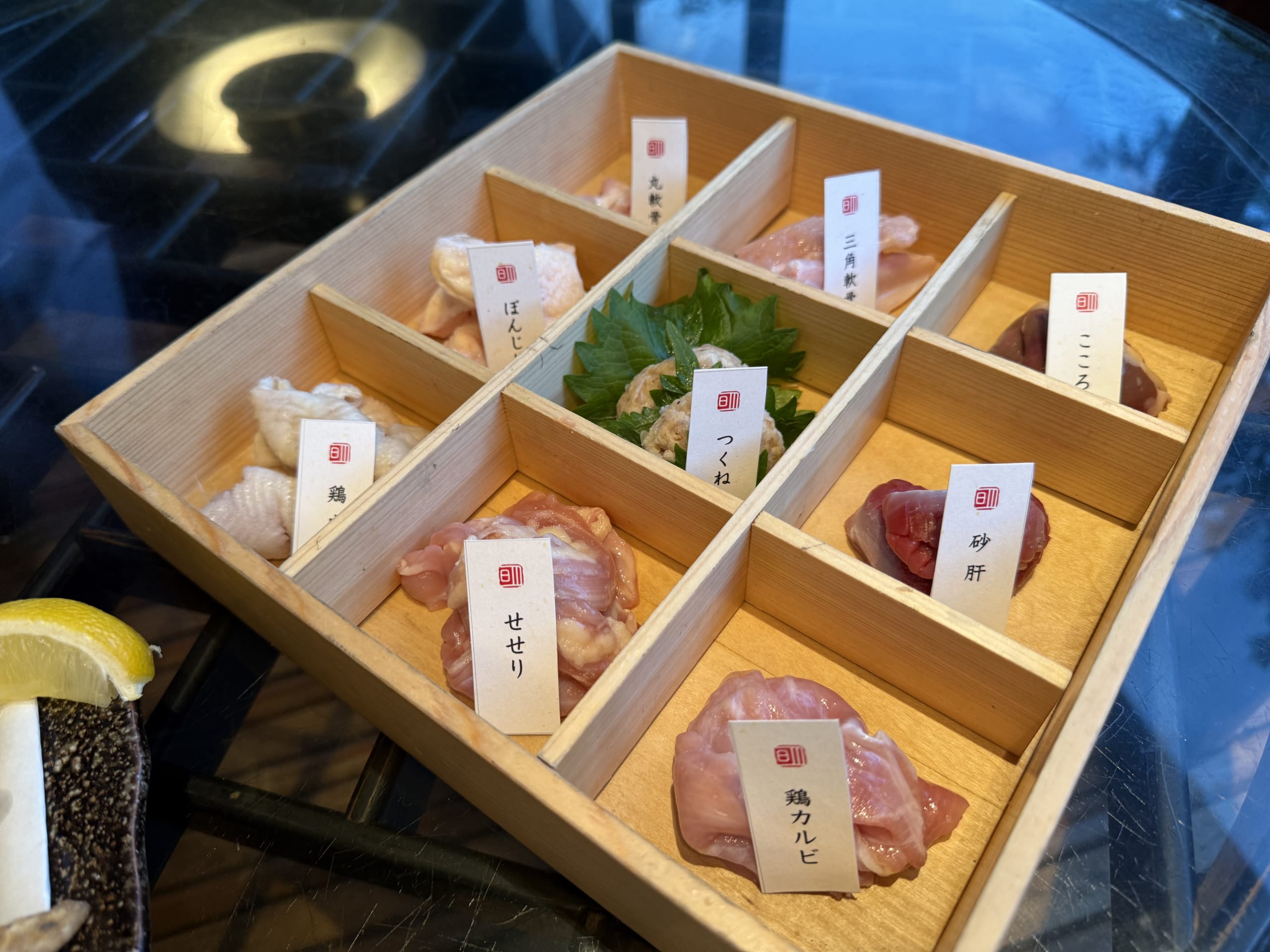 黒い鉄板の上で焼かれた、串に刺さない焼き鳥の盛り合わせ。様々な部位の鶏肉とネギが盛り付けられている。