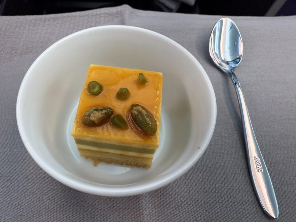 白い皿に乗ったピスタチオのレイヤーケーキの一切れ。鮮やかな緑色のクリームの上に、刻んだピスタチオと赤いベリーが飾られている。