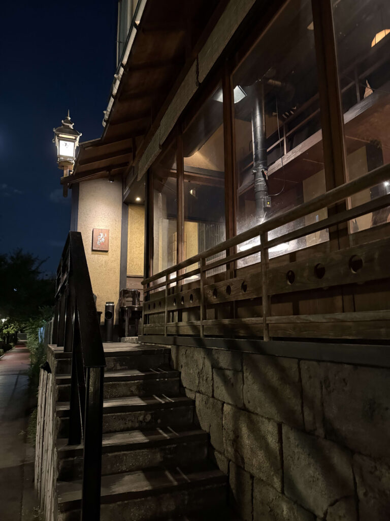 The exterior of Yakitori Akira Meguro Honten at night. It's a Japanese-style corner building with a large, illuminated white lantern bearing the restaurant's name at the entrance.
