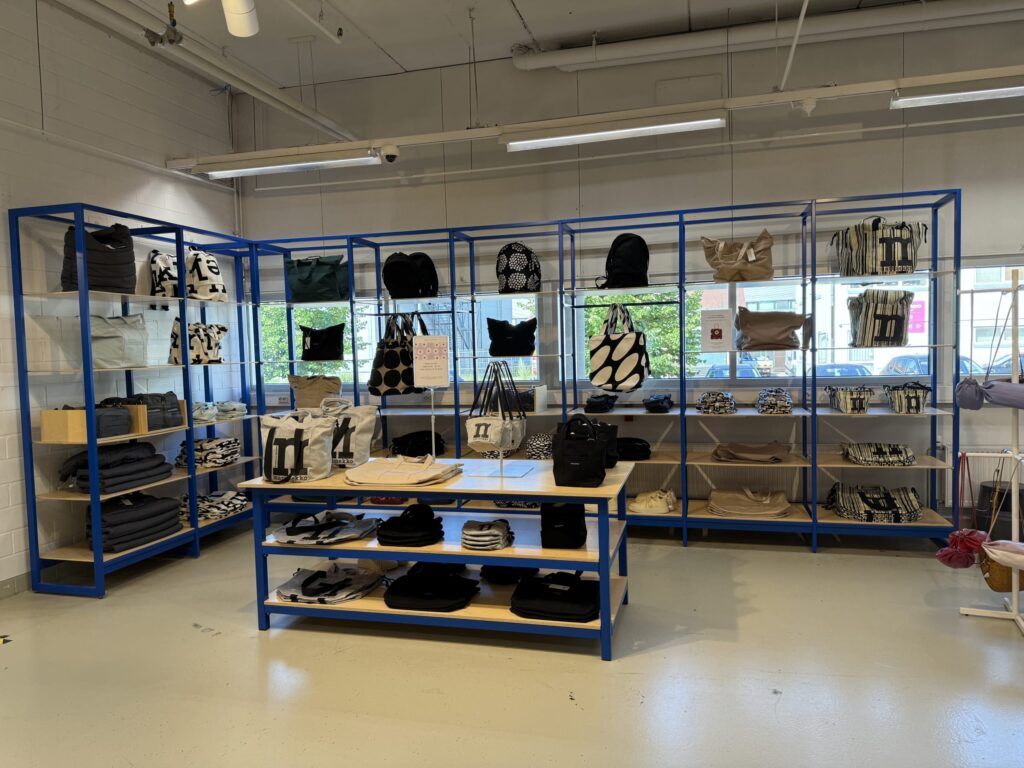 The interior of a Marimekko store, showing a variety of bags and accessories displayed on blue metal and wood shelving units.
