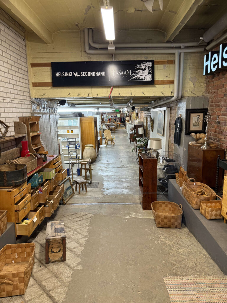 The interior of a secondhand shop in Helsinki. A long aisle lined with vintage furniture and wooden baskets stretches into the back of the store.